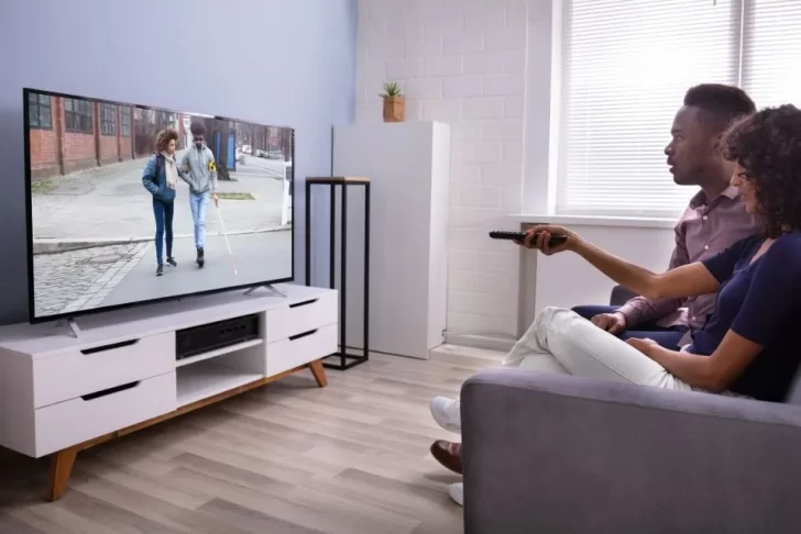 casal assistindo televisão em frente ao painel/rack.